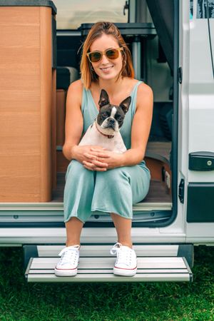 Woman sitting on stoop of motorhome door with cute dog on her lap, vertical