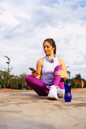 Young woman sitting on sports ground while browsing smartphone