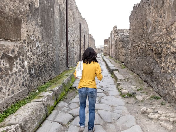 Rear view of a woman in yellow clothes walking while exploring ancient ruins