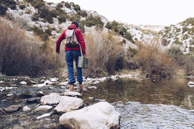 Woman with case jumping on rocks above stream