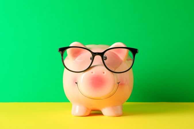 Happy piggy bank with glasses on color table against green background, space for text. Finance, saving money