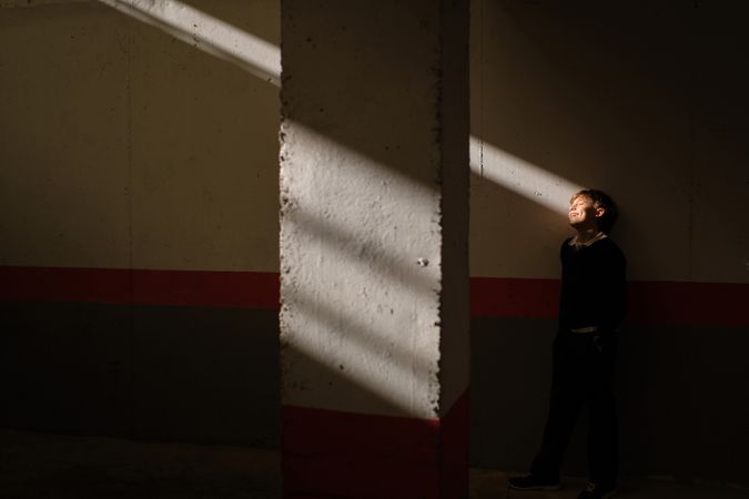Adorable preteen boy standing near wall in sunbeam