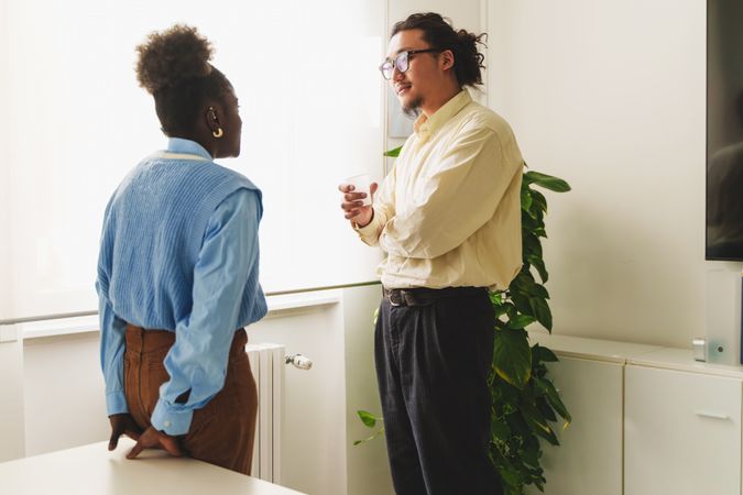 An Asian man and Black woman engage in a casual conversation in an office setting