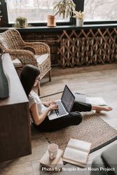Side view of woman working on her laptop sitting on floor at home 0LWYgb