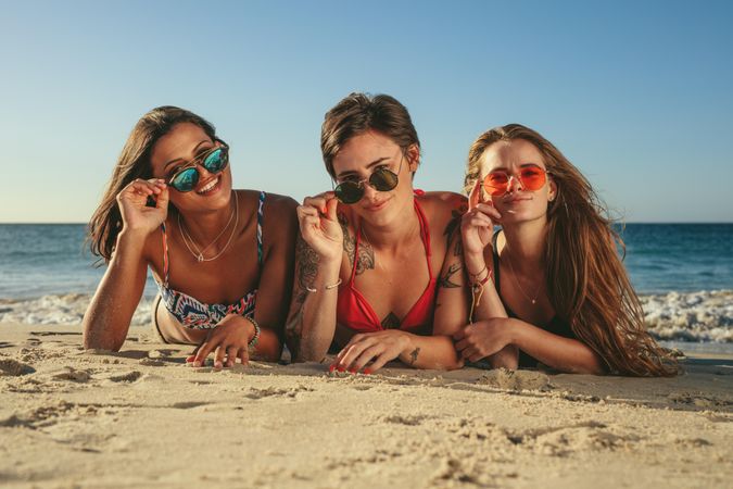 Group of women lying on the beach sand wearing colorful sunglasses