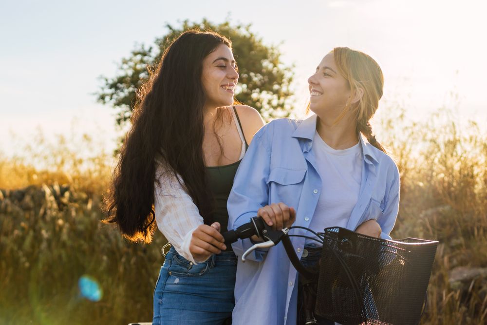 two young women on a bike in a field during sunset