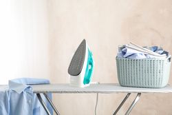 Iron and basket with clear laundry against light background, space for text