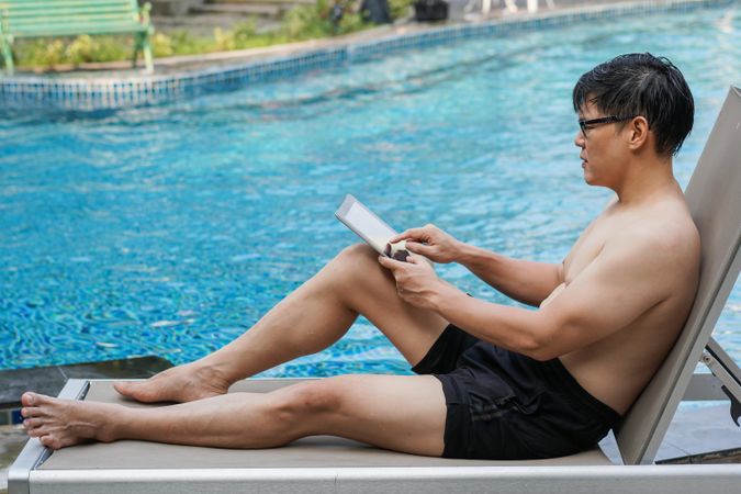 Man with digital tablet sitting by the pool