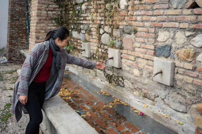 Young woman in casual clothing washing hands in street fountain