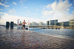 Athletic man running next to the river outside without a shirt