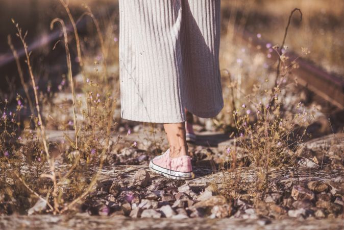 Long haired woman standing on railways overgrown with dry grass