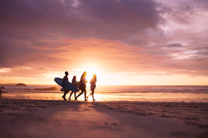 Group of young surfers walking along beach at sunset
