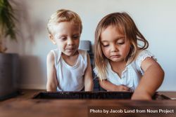 Little girl looking into an old wooden box with her brother sitting by 48GQ75