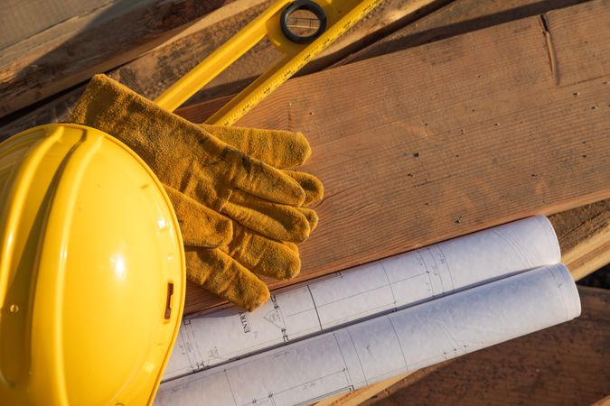 Abstract of Constrcution Hard Hat, Gloves, Level and House Plans Resting on Wood Planks