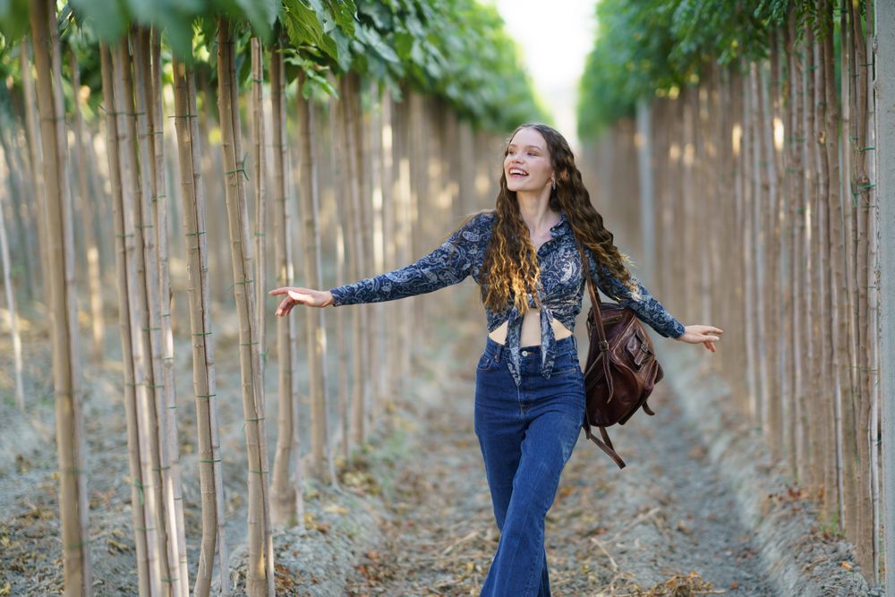 A Joyful Young Woman Happily Walking Among Tall Trees in Beautiful Nature Surroundings
