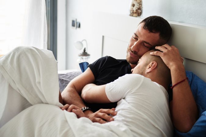 Smiling gay couple hugging on bed