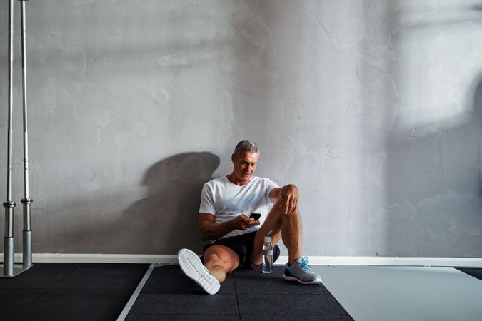 Man checking his cell phone resting against wall after workout
