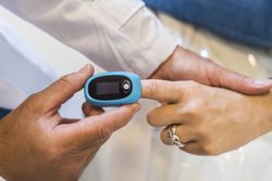 Doctor is putting a pulse oximeter in his patient's hand for measuring oxygen saturation in blood and heart rate.