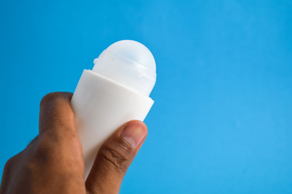 Hand holding a round deodorant bottle on blue background