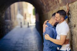Man resting his head on his partners shoulder under a city bridge