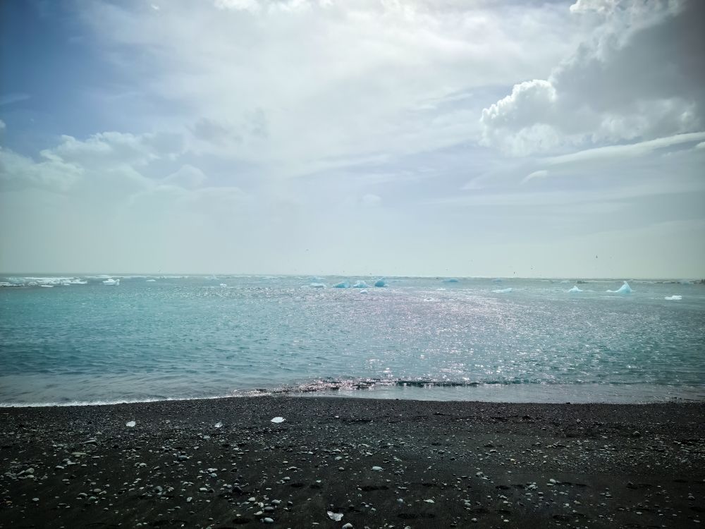 Diamond Beach in Iceland with blue icebergs melting on sand and ice glistening with sunlight.