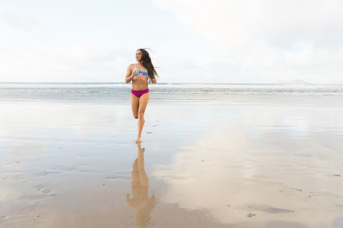 Woman in swimwear running near sea
