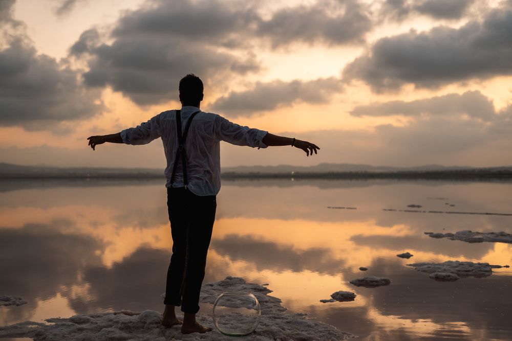 Relaxed man standing with outstretched hands with empty fish tank at shore