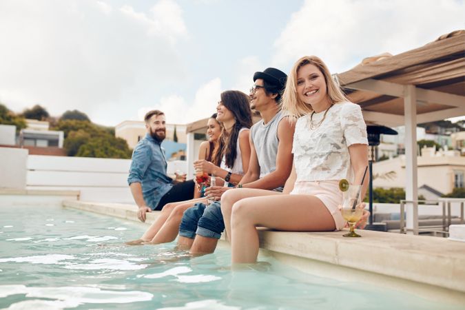 Young people relaxing by the swimming pool with their feet in water