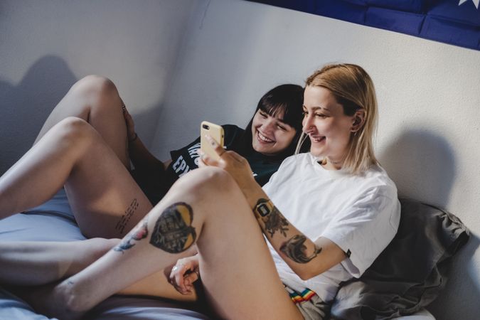 Happy lesbian couple using smartphone on bed