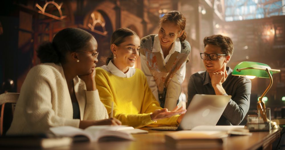 Diverse Group of Students Collaborating on a Project in a Warmly Lit Library.