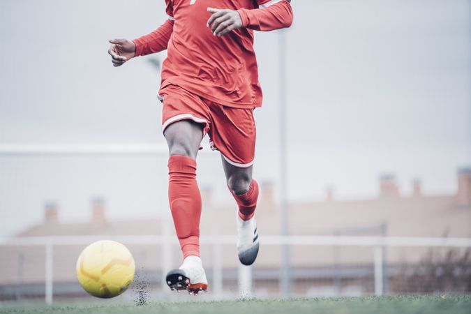 Black soccer player with red outfit playing soccer.