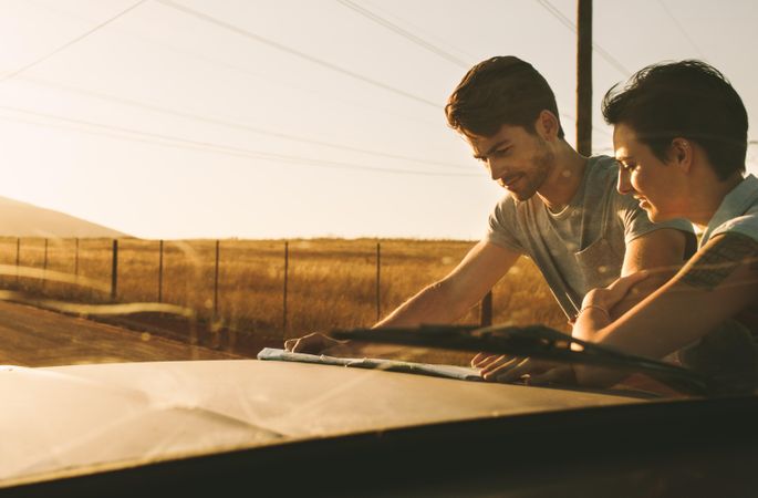 Young man and woman looking at map on hood of truck parked on dirt road