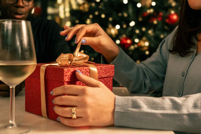 Close-up of a woman's hands opening a red Christmas gift box at a party