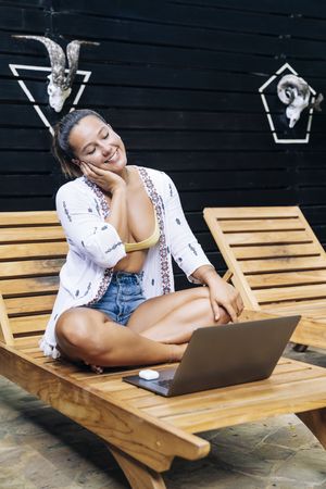 Relaxed woman using laptop while resting on deck chair