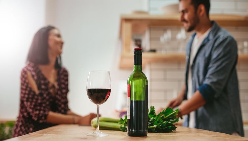 Man and woman talking in kitchen with wine glass in focus