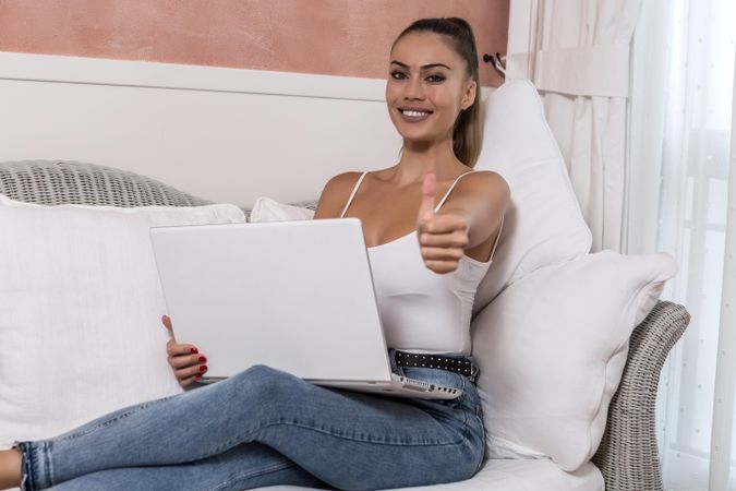 Smiling woman using computer with thumb up sitting on couch