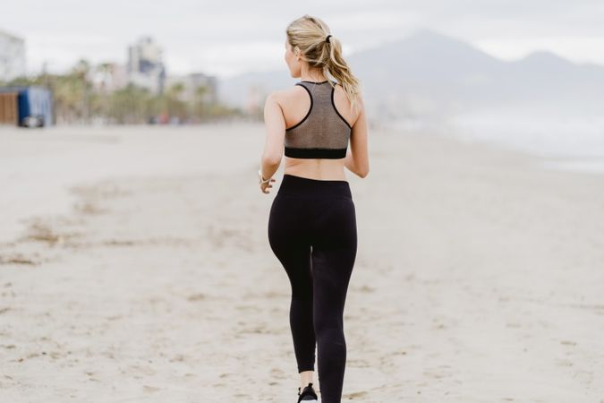 Female runner in stylish sportswear jogging along calm sandy seaside