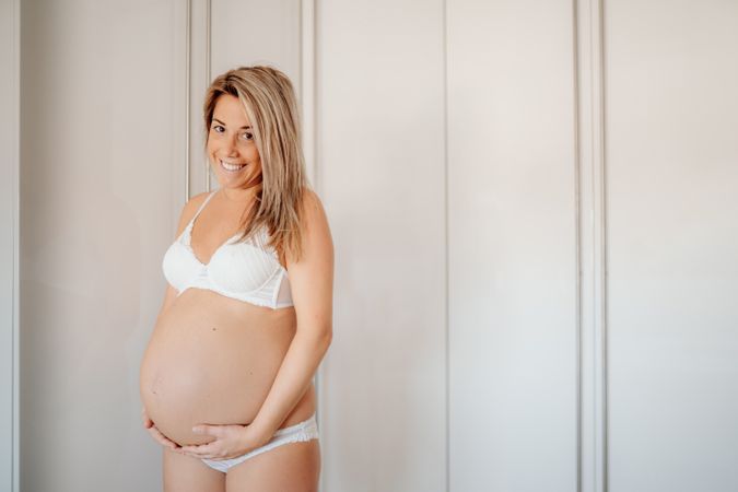 Smiling pregnant woman touching naked abdomen