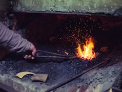 Crop faceless farrier melting metal in furnace in smithy