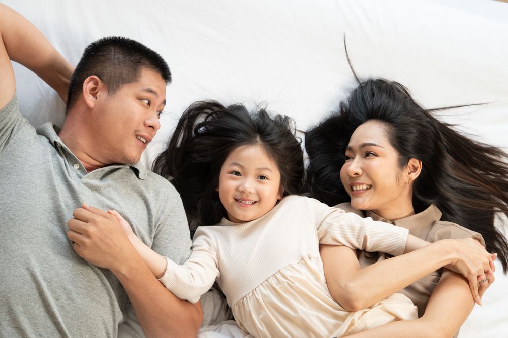 Top view of Asian family lying on bed and holding hands together.