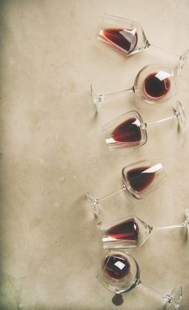 Glasses of red wine glasses laying on grey background, vertical composition with copy space