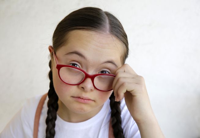 Portrait of young girl looking at camera while holding her eyeglasses away from eyes