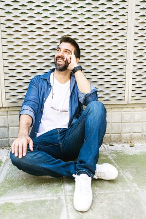 Happy Latino man in denim relaxing on pavement outside