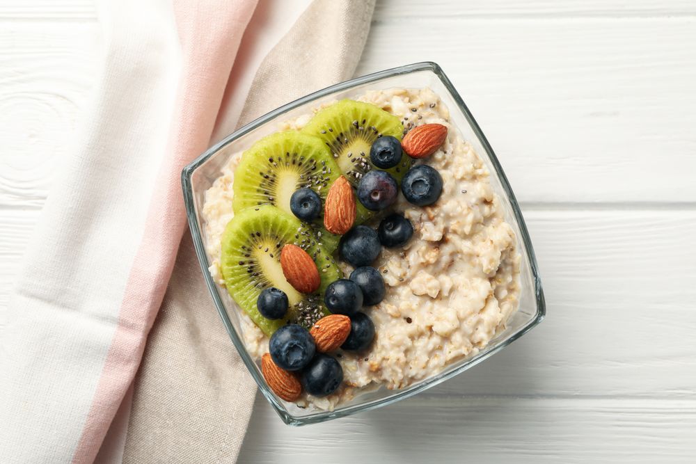 Towel and bowl with oatmeal porridge and fruits on wooden background