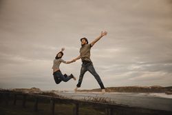 Couple holding hands and jumping on bench on shore near water