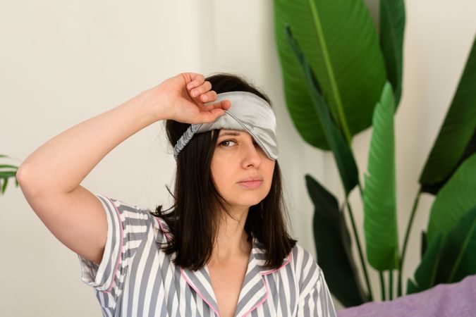 Woman adjusting sleep mask, with tropical plants in background.