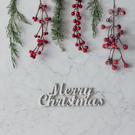 Christmas branches and berries on marble table with “Merry Christmas”