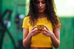 Woman with curly hair in yellow t-shirt and jeans texting on phone
