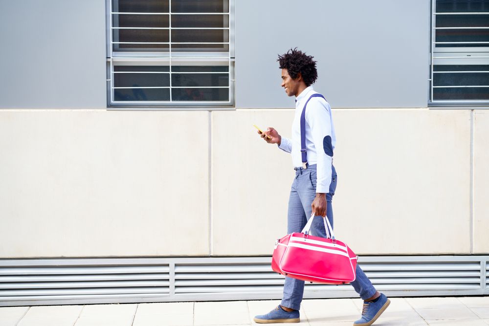Side view of male with curly hair wearing shirt and suspenders walking on street
