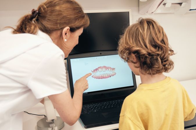 Female dentist explaining 3D teeth scan to faceless boy